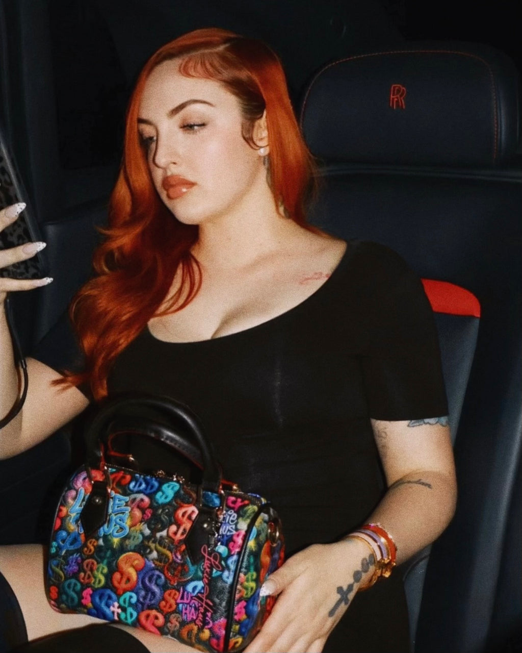 Woman holding Luxie Haus Rich Girl Mini handbag with colorful money print inside luxury car